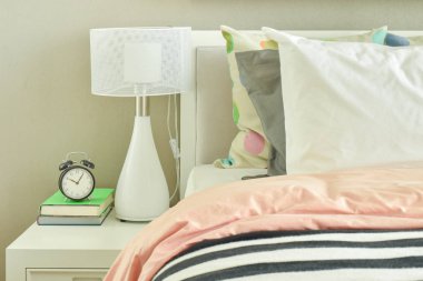 Saat ve çizgili yatak yanında beyaz masa lambası