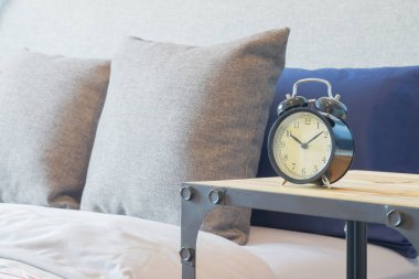 Yatak yastık ile yanındaki ahşap masa retro tarzı çalar saat