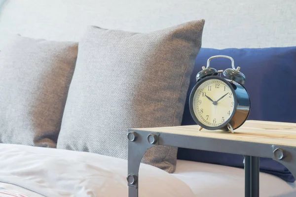 Reloj despertador de estilo retro en mesa de madera junto a la cama con almohadas — Foto de Stock