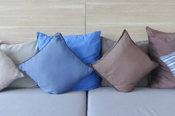 Almohadas azules y marrones yacen en sofá azul claro con pared de madera en el fondo . — Foto de Stock