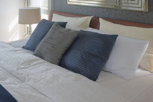 Almohadas grises y azules profundas en la cama y lámpara de lectura blanca en el fondo —  Fotos de Stock