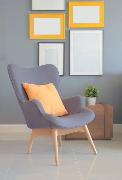 Retry style armchair with orange pillow in living room with wall of picture frame in background