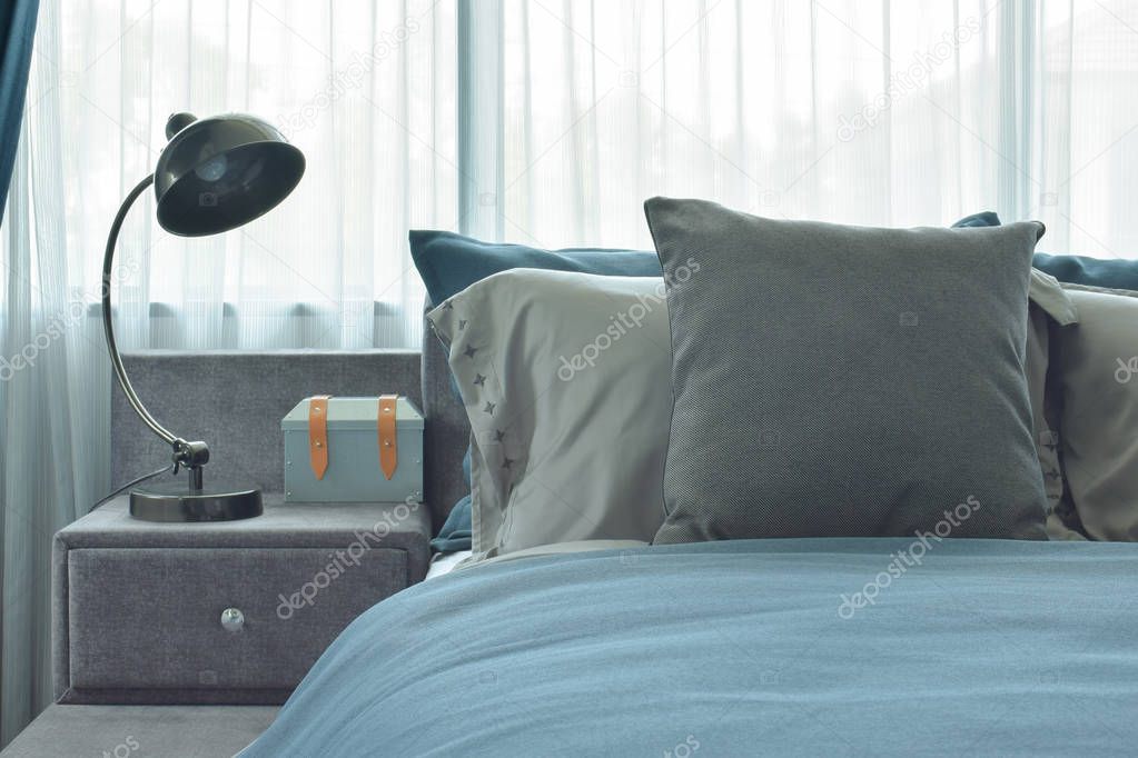 Gray and deep blue pillows setting on bed with industrial style reading lamp next to bed