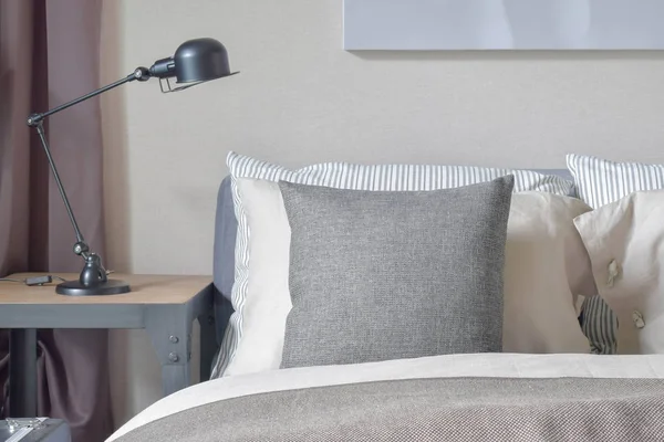 Almohadas grises, beige y peladas colocadas en la cama con lámpara de lectura negra en la mesa de noche —  Fotos de Stock