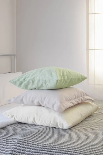 Stack of pastel color pillows on stripe blanket on bed