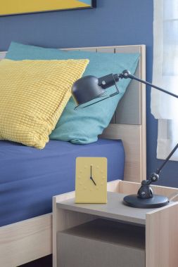 Yellow modern clock on bedside table with colorful pillows in background clipart