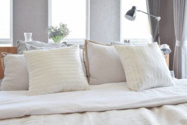 Beyaz çizgili yastık yatak ve dekoratif masa lambası ile şık yatak odası iç tasarım.