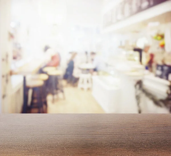 Wooden table top with blur of coffee shop interior as background — Stock Photo, Image