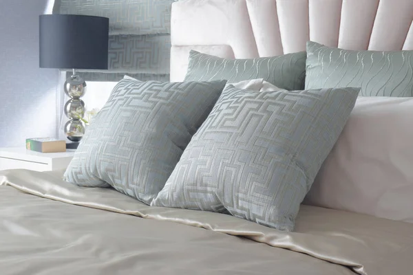 Light blue satin finished pillows on bed and black reading lamp in background