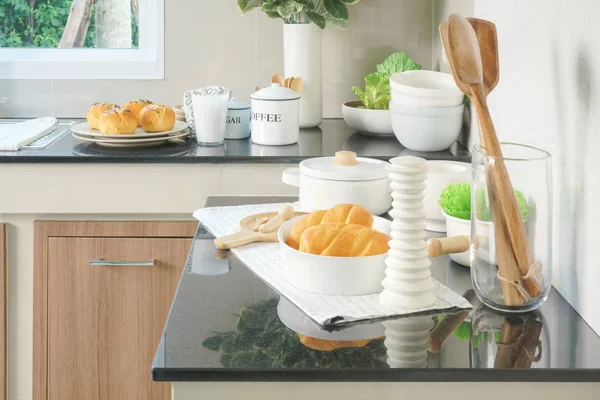 Brötchen, Brot und weißes Keramikgeschirr auf schwarzer Arbeitsplatte in der Küche — Stockfoto