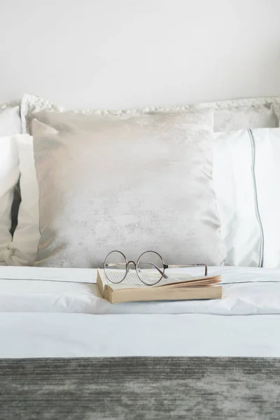 Vidros e livro na cama com almofadas acabadas de veludo no fundo — Fotografia de Stock