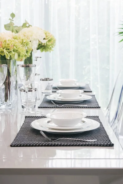 Porslin och glas inställning på matbord med vita och gröna blommor i mitten av tabellen — Stockfoto