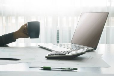 muhasebeci hesap makinesi ve ahşap masa üstünde laptop araçlarıyla, erkek fincan kahve arka plan, mali ve iş kavramı tutan eller.