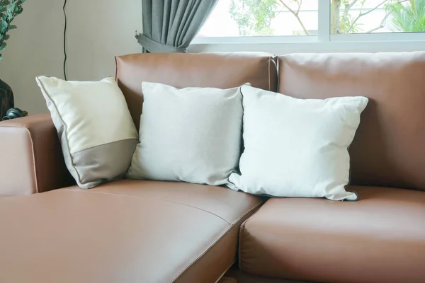 Sofá de cuero marrón claro con almohadas junto a la ventana en la sala de estar — Foto de Stock