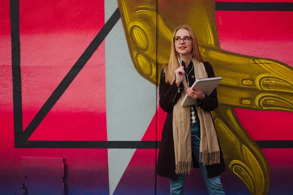 Jeune fille blonde en lunettes de soleil posant près d'un mur coloré, écouteurs et montre intelligente — Photo