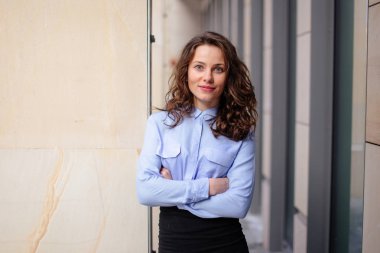 Kameraya dört gözle bina, duvara yakın duran esmer gülümseyen kadın