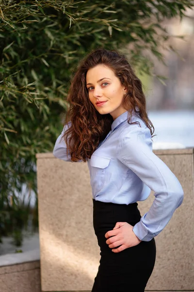 Morena sonriente mujer de pie cerca de la pared del edificio, mirando hacia adelante en la cámara — Foto de Stock