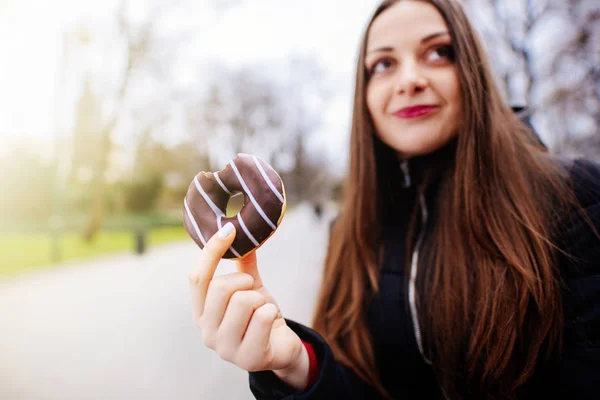 Mooi meisje eten donut op park achtergrond en glimlach — Stockfoto