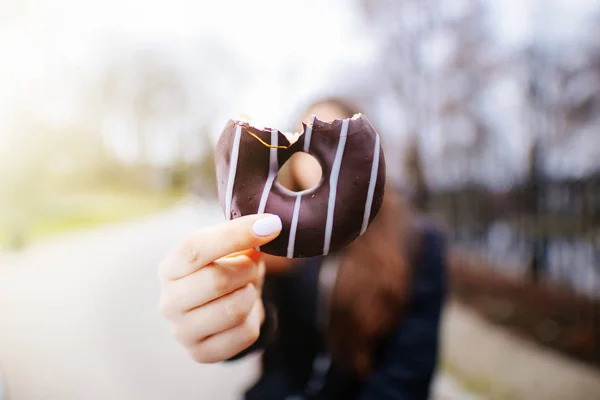 Mooi meisje eten donut op park achtergrond en glimlach — Stockfoto