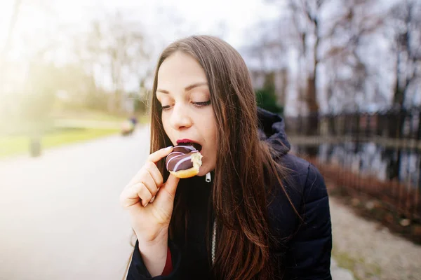 Mooi meisje eten donut op park achtergrond en glimlach — Stockfoto