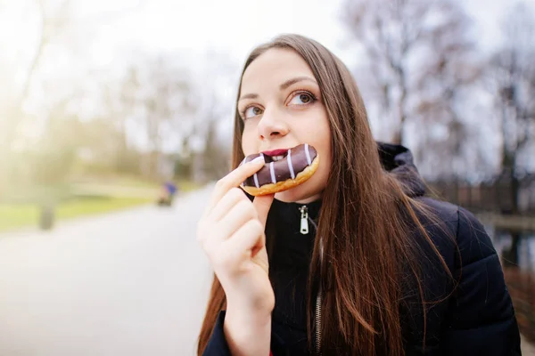 Mooi meisje eten donut op park achtergrond en glimlach — Stockfoto