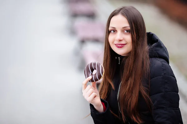 Jeune jolie fille manger beignet au fond du parc et sourire — Photo