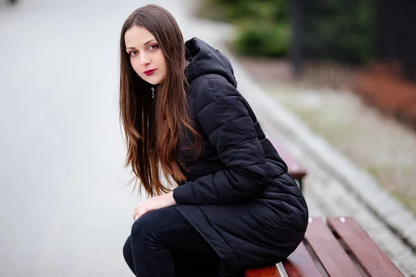 Junge Frau sitzt auf der Bank und lächelt in die Kamera — Stockfoto