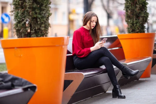 Брюнетка сидит на улице и пишет смс по телефону — стоковое фото