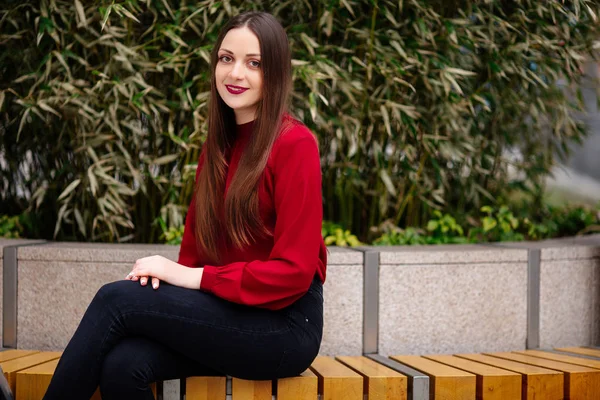 Jovem mulher sentada no banco e sorrindo para a câmera — Fotografia de Stock