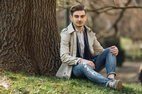 Модний чоловік сидить біля дерев з розмитим фоном — стокове фото