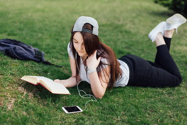 Söt flicka läsa bok och lyssna på musik på park — Stockfoto