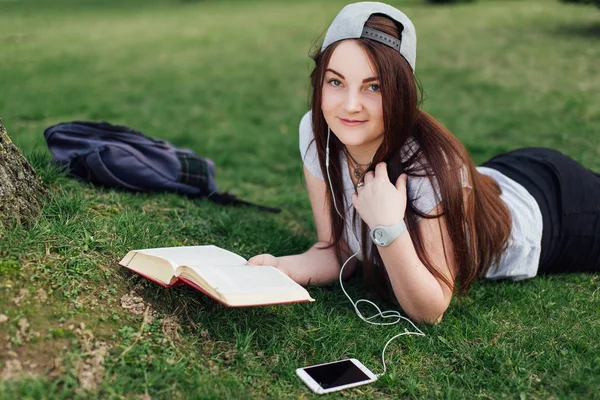 Söt flicka läsa bok och lyssna på musik på park — Stockfoto