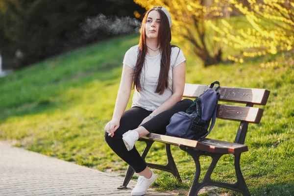 年轻女孩烟香烟在日落公园 — 图库照片