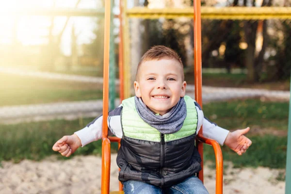 Petit garçon jouer sur l'aire de jeux avec fond de parc flou — Photo