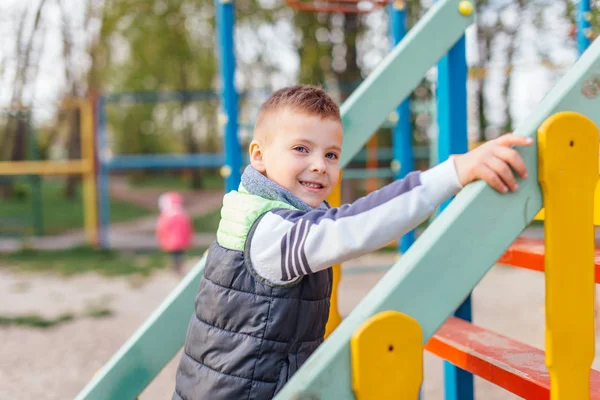 Mały chłopiec grać na placu zabaw z rozmycie tła park — Zdjęcie stockowe