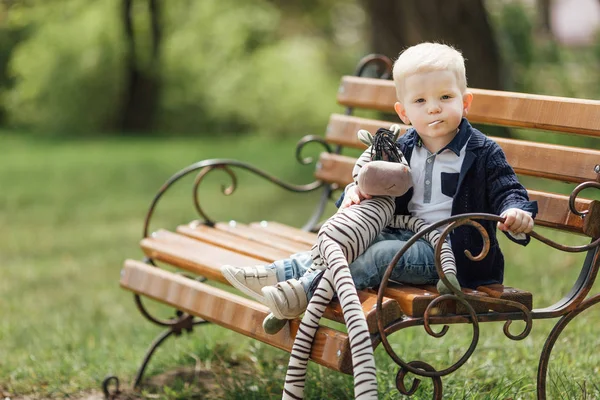 小さな男の子彼のおもちゃでベンチの上に座る — ストック写真