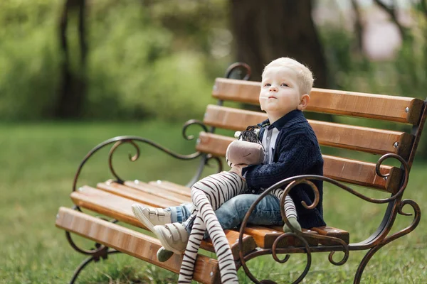 小さな男の子彼のおもちゃでベンチの上に座る — ストック写真