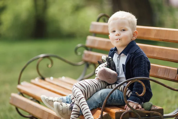 Menino se senta no banco com seu brinquedo — Fotografia de Stock