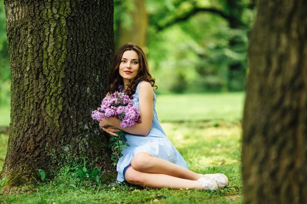 Jeune fille debout au fond du parc avec bouquet de fleurs — Photo