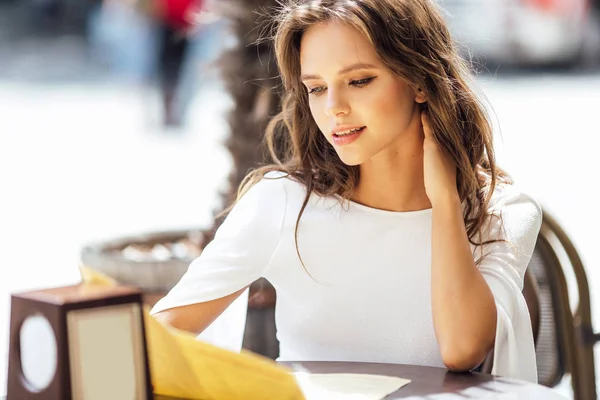 Menina bonita sentar-se à mesa e escolher uma refeição — Fotografia de Stock