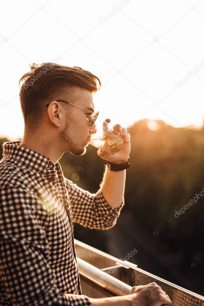 Stylish man sit on the table and drink whiskey