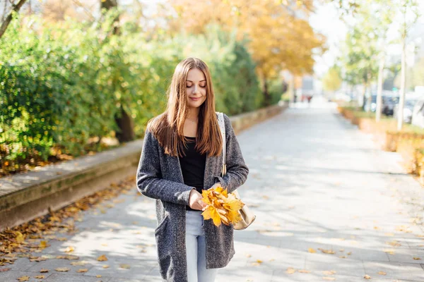 Ung kvinna kasta löv på gatan — Stockfoto