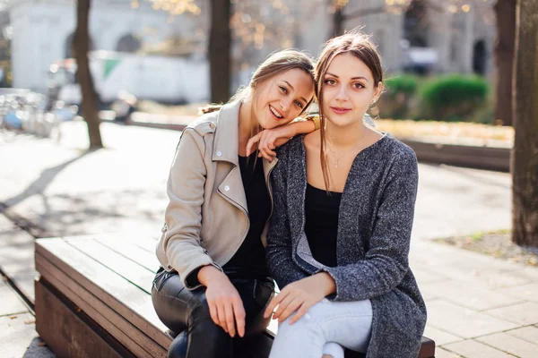 Duas meninas sentam-se no banco e riem para a câmera — Fotografia de Stock