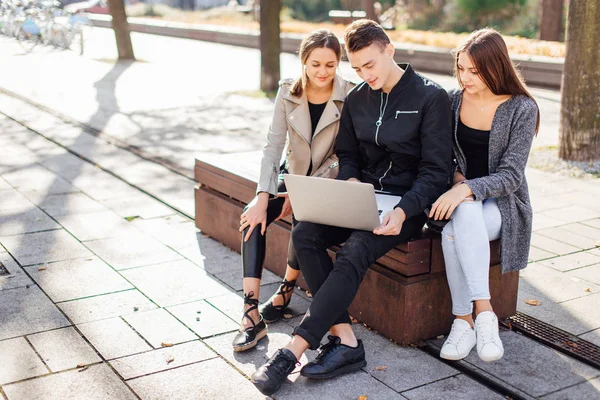 Três amigos sentam-se no banco com laptop — Fotografia de Stock