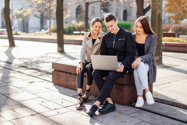Три друга сидят на скамейке с ноутбуком — стоковое фото