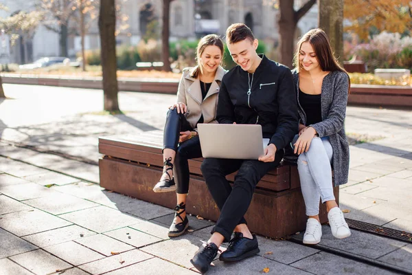 Três amigos sentam-se no banco com laptop — Fotografia de Stock