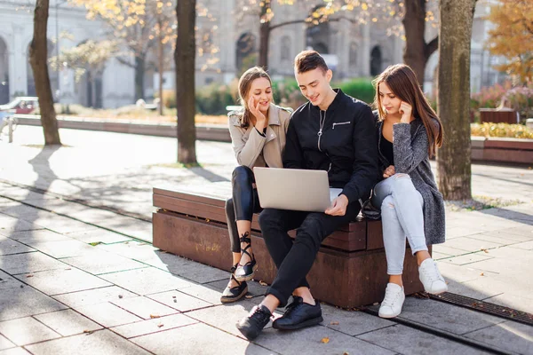 Três amigos sentam-se no banco com laptop — Fotografia de Stock