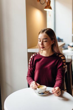 Genç kız oturup fincan kahve ve kamera için bir gülümseme ile