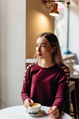 Genç kız oturup fincan kahve ve kamera için bir gülümseme ile