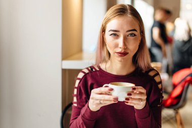 Genç kız oturup fincan kahve ve kamera için bir gülümseme ile